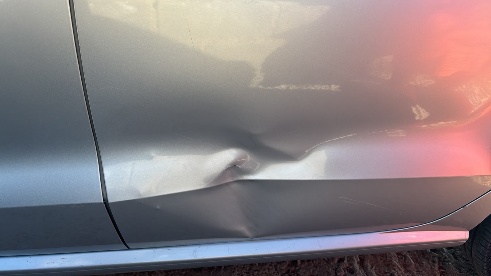 Close-up of impact dent damage on a silver car door